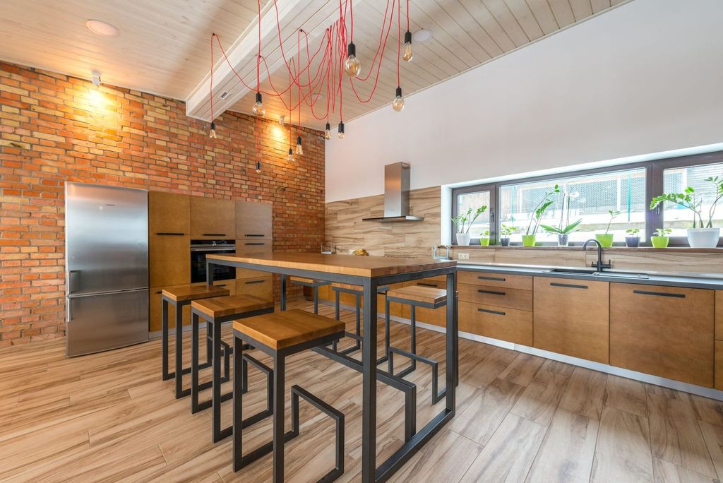 Cuisine de loft : brique, bois et acier, îlot éclairé par des suspensions.